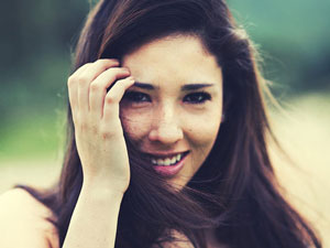 brunette girl with long hair smiling while brushing hair back with hand