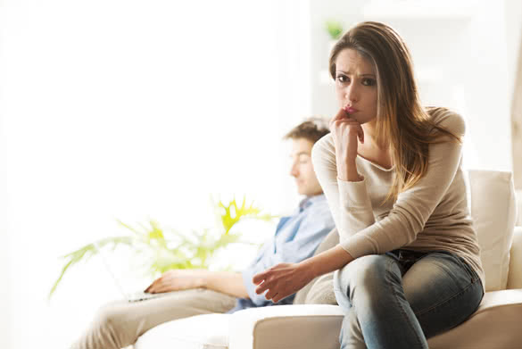 Sad woman close-up with her boyfriend on background sitting on sofa